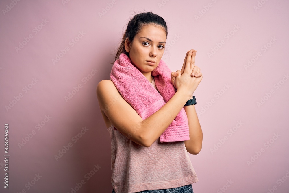 Young beautiful brunette sportswoman wearing sportswear and towel over pink background Holding symbolic gun with hand gesture, playing killing shooting weapons, angry face Young beautiful brunette sportswoman wearing sportswear and towel over pink background Holding symbolic gun with hand gesture, playing killing shooting weapons, angry face