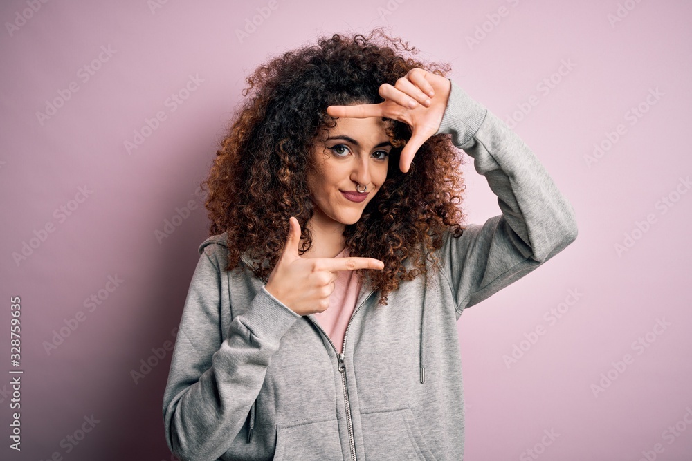 Young beautiful brunette sportswoman with curly hair and piercing wearing sportswear smiling making frame with hands and fingers with happy face. Creativity and photography concept. Young beautiful brunette sportswoman with curly hair and piercing wearing sportswear smiling making frame with hands and fingers with happy face. Creativity and photography concept.