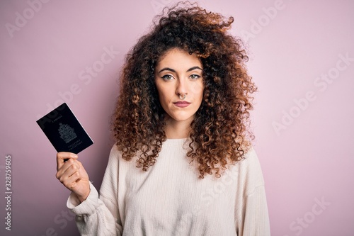 Beautiful tourist woman with curly hair and piercing holding canada canadian passport id with a confident expression on smart face thinking serious