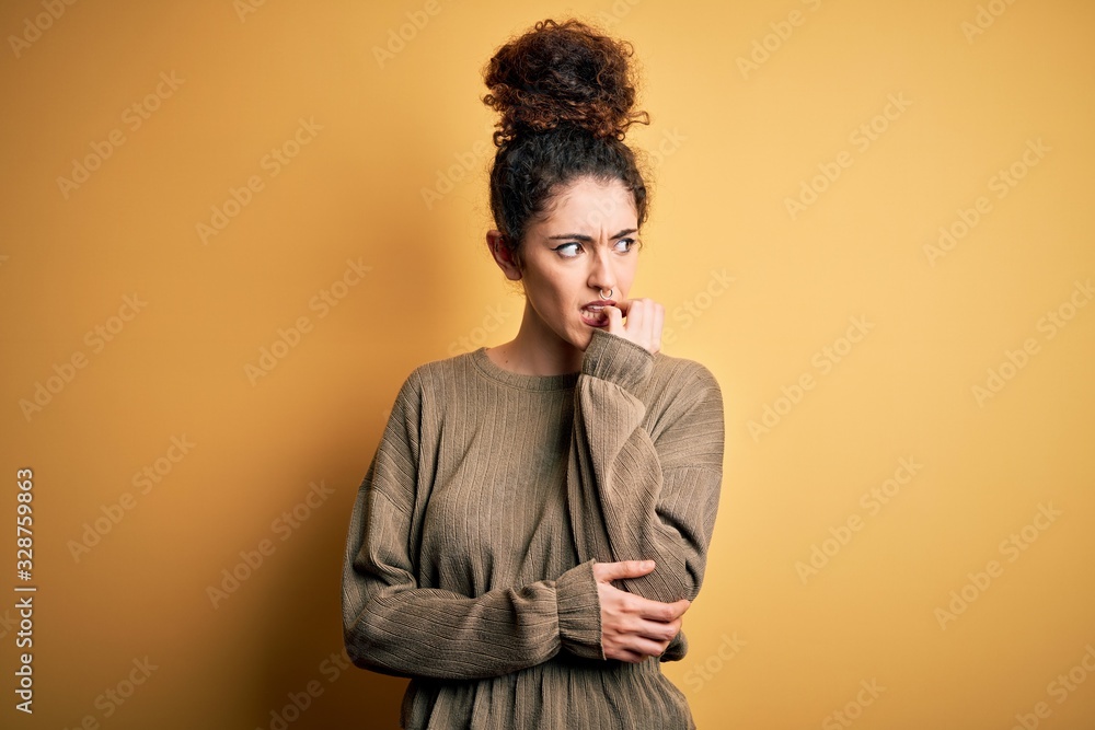 Young beautiful brunette woman with curly hair and piercing wearing casual dress looking stressed and nervous with hands on mouth biting nails. Anxiety problem. Young beautiful brunette woman with curly hair and piercing wearing casual dress looking stressed and nervous with hands on mouth biting nails. Anxiety problem.