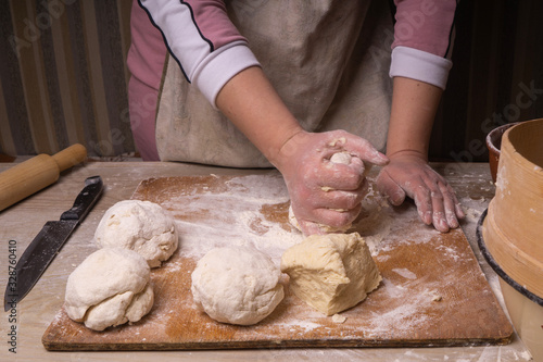 A woman kneads the dough. Plywood cutting board, wooden flour sieve and wooden rolling pin - tools for making dough.