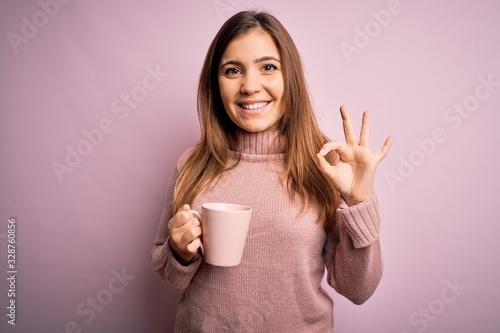 Young blonde woman drinking a cup of coffee over pink isolated background doing ok sign with fingers  excellent symbol