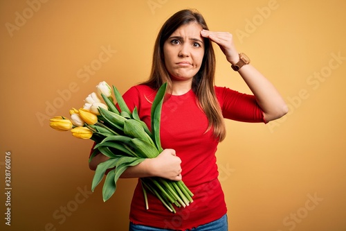 Young blonde woman holding romantic bouquet of tulips flowers over yellow background worried and stressed about a problem with hand on forehead  nervous and anxious for crisis