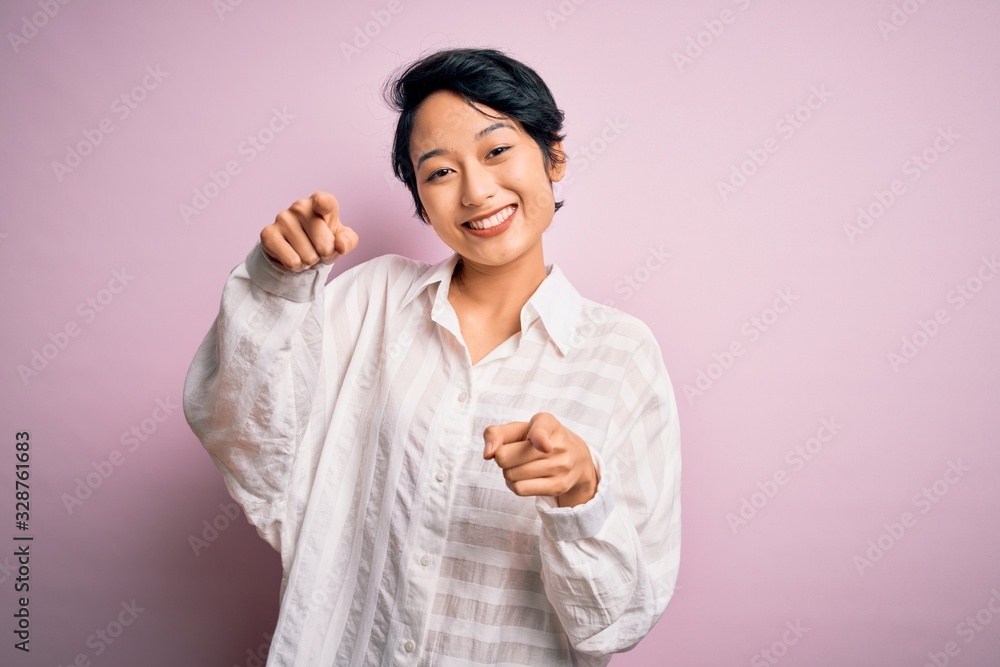 Young beautiful asian girl wearing casual shirt standing over isolated pink background pointing to you and the camera with fingers, smiling positive and cheerful Young beautiful asian girl wearing casual shirt standing over isolated pink background pointing to you and the camera with fingers, smiling positive and cheerful
