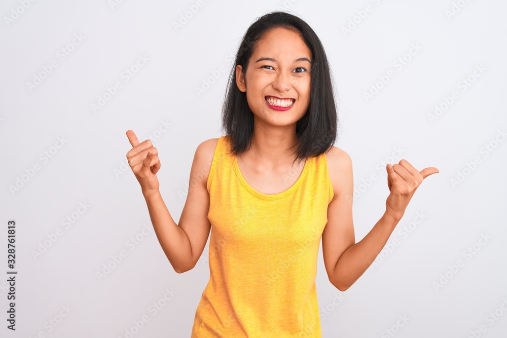 Young chinese woman wearing yellow casual t-shirt standing over isolated white background shouting with crazy expression doing rock symbol with hands up. Music star. Heavy concept. Young chinese woman wearing yellow casual t-shirt standing over isolated white background shouting with crazy expression doing rock symbol with hands up. Music star. Heavy concept.