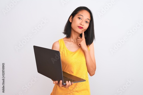 Young beautiful chinese woman using laptop standing over isolated white background serious face thinking about question, very confused idea