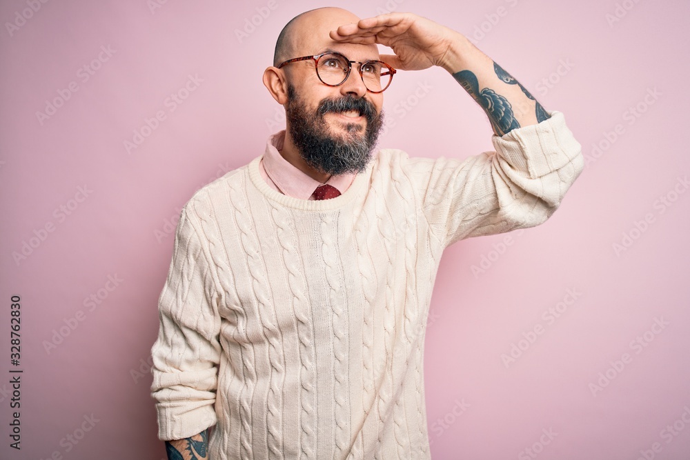 Φωτογραφία Handsome bald man with beard and tattoo wearing glasses and sweater over pink background very happy and smiling looking far away with hand over head