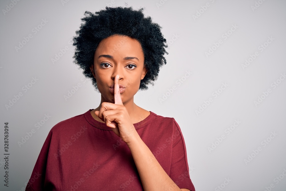 Young beautiful African American afro woman with curly hair wearing casual t-shirt standing asking to be quiet with finger on lips. Silence and secret concept. Young beautiful African American afro woman with curly hair wearing casual t-shirt standing asking to be quiet with finger on lips. Silence and secret concept.