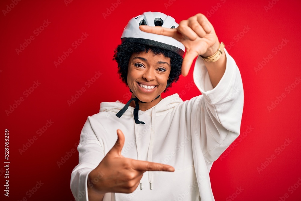 Young African American afro cyciling woman with curly hair wearing bike security helmet smiling making frame with hands and fingers with happy face. Creativity and photography concept. Young African American afro cyciling woman with curly hair wearing bike security helmet smiling making frame with hands and fingers with happy face. Creativity and photography concept.