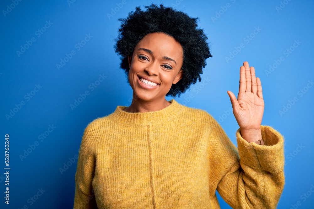 Young beautiful African American afro woman with curly hair wearing yellow casual sweater Waiving saying hello happy and smiling, friendly welcome gesture Young beautiful African American afro woman with curly hair wearing yellow casual sweater Waiving saying hello happy and smiling, friendly welcome gesture