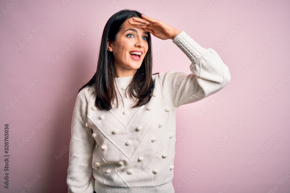 Young brunette woman with blue eyes wearing casual sweater over isolated pink background very happy and smiling looking far away with hand over head. Searching concept. Young brunette woman with blue eyes wearing casual sweater over isolated pink background very happy and smiling looking far away with hand over head. Searching concept.