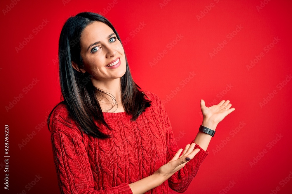 Young brunette woman with blue eyes wearing casual sweater over isolated red background Inviting to enter smiling natural with open hand Young brunette woman with blue eyes wearing casual sweater over isolated red background Inviting to enter smiling natural with open hand