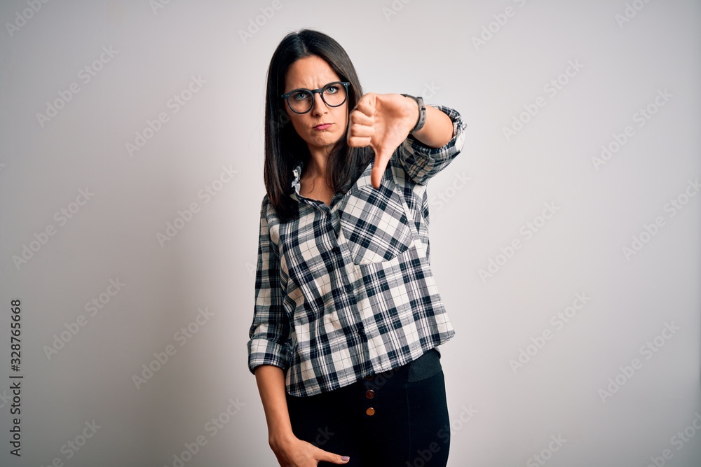 Young brunette woman with blue eyes wearing casual shirt and glasses over white background looking unhappy and angry showing rejection and negative with thumbs down gesture. Bad expression. Young brunette woman with blue eyes wearing casual shirt and glasses over white background looking unhappy and angry showing rejection and negative with thumbs down gesture. Bad expression.