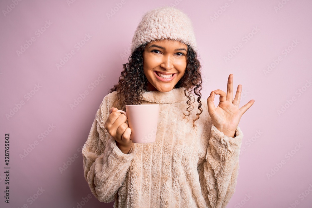 Young beautiful woman with curly hair drinking mug of coffee over isolated pink background doing ok sign with fingers, excellent symbol Young beautiful woman with curly hair drinking mug of coffee over isolated pink background doing ok sign with fingers, excellent symbol