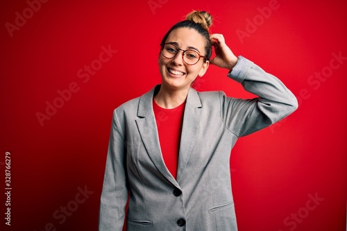 Young beautiful blonde businesswoman with blue eyes wearing glasses and jacket confuse and wonder about question. Uncertain with doubt, thinking with hand on head. Pensive concept. © Krakenimages.com