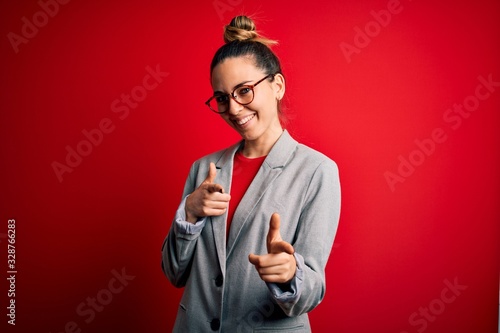 Young beautiful blonde businesswoman with blue eyes wearing glasses and jacket pointing fingers to camera with happy and funny face. Good energy and vibes. © Krakenimages.com