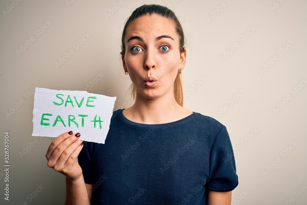 Young beautiful woman holding paper asking for save earth and enviroment conservation scared in shock with a surprise face, afraid and excited with fear expression Young beautiful woman holding paper asking for save earth and enviroment conservation scared in shock with a surprise face, afraid and excited with fear expression