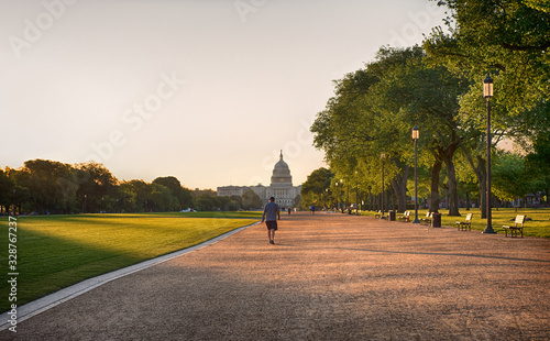 A man dressed in T shirt, shorts and cap taking a brisk walk, away from the camera, through the National Mall, Washington DC photo