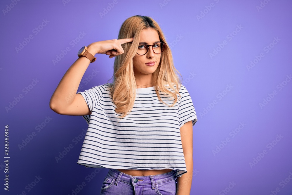 Young beautiful blonde woman wearing striped t-shirt and glasses over purple background pointing unhappy to pimple on forehead, ugly infection of blackhead. Acne and skin problem Young beautiful blonde woman wearing striped t-shirt and glasses over purple background pointing unhappy to pimple on forehead, ugly infection of blackhead. Acne and skin problem