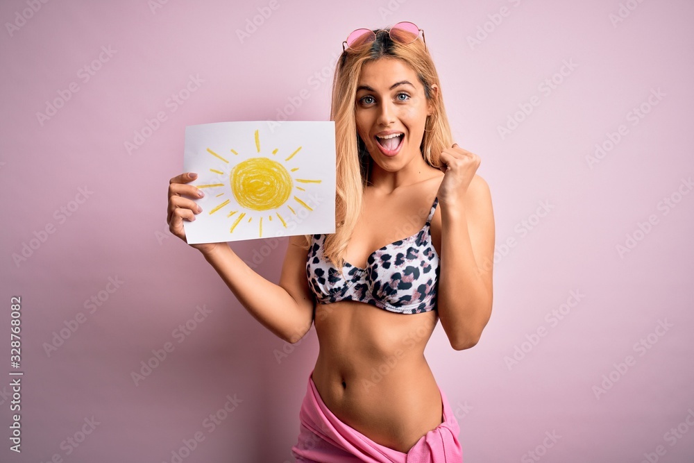 Young beautiful blonde woman on vacation wearing bikini holding banner with sun draw screaming proud and celebrating victory and success very excited, cheering emotion Young beautiful blonde woman on vacation wearing bikini holding banner with sun draw screaming proud and celebrating victory and success very excited, cheering emotion