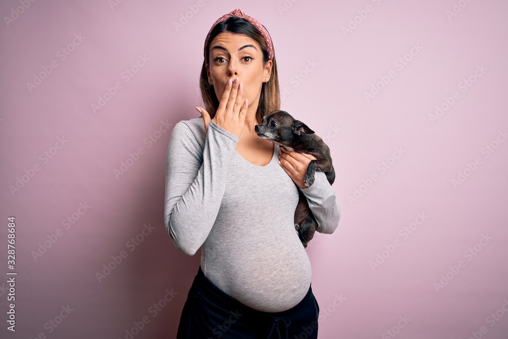 Young beautiful brunette woman pregnant expecting baby holding chihuahua puppy cover mouth with hand shocked with shame for mistake, expression of fear, scared in silence, secret concept