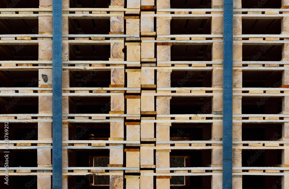 Close-up, texture and background of many wooden pallets stacked on top of one another and held together by tension belts