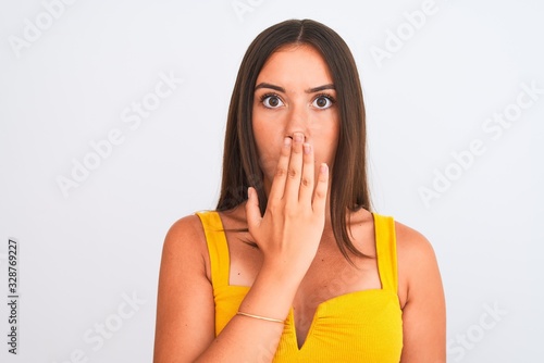 Young beautiful girl wearing yellow casual t-shirt standing over isolated white background cover mouth with hand shocked with shame for mistake, expression of fear, scared in silence, secret concept