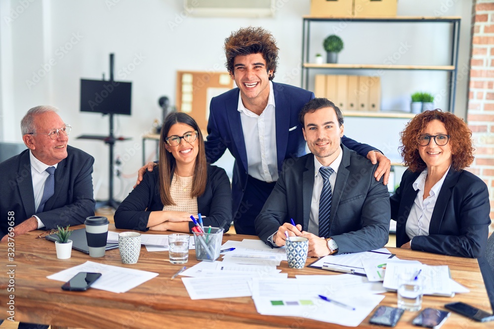 Group of business workers smiling happy and confident in a meeting. The boss standing and employees sitting with smile on face looking at the camera at the office Group of business workers smiling happy and confident in a meeting. The boss standing and employees sitting with smile on face looking at the camera at the office