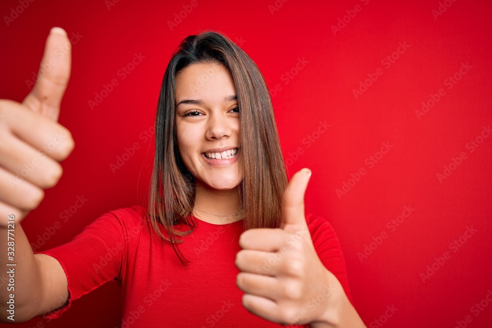 Young beautiful brunette girl wearing casual t-shirt over isolated red background approving doing positive gesture with hand, thumbs up smiling and happy for success. Winner gesture. Young beautiful brunette girl wearing casual t-shirt over isolated red background approving doing positive gesture with hand, thumbs up smiling and happy for success. Winner gesture.
