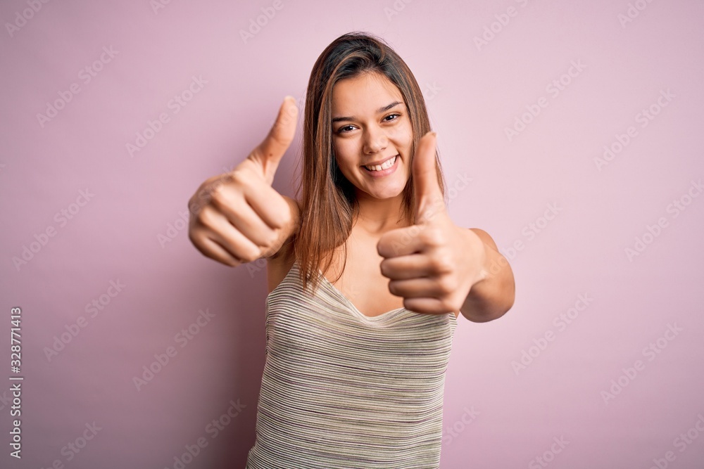 Young beautiful brunette girl wearing casual striped t-shirt over isolated pink background approving doing positive gesture with hand, thumbs up smiling and happy for success. Winner gesture. Young beautiful brunette girl wearing casual striped t-shirt over isolated pink background approving doing positive gesture with hand, thumbs up smiling and happy for success. Winner gesture.