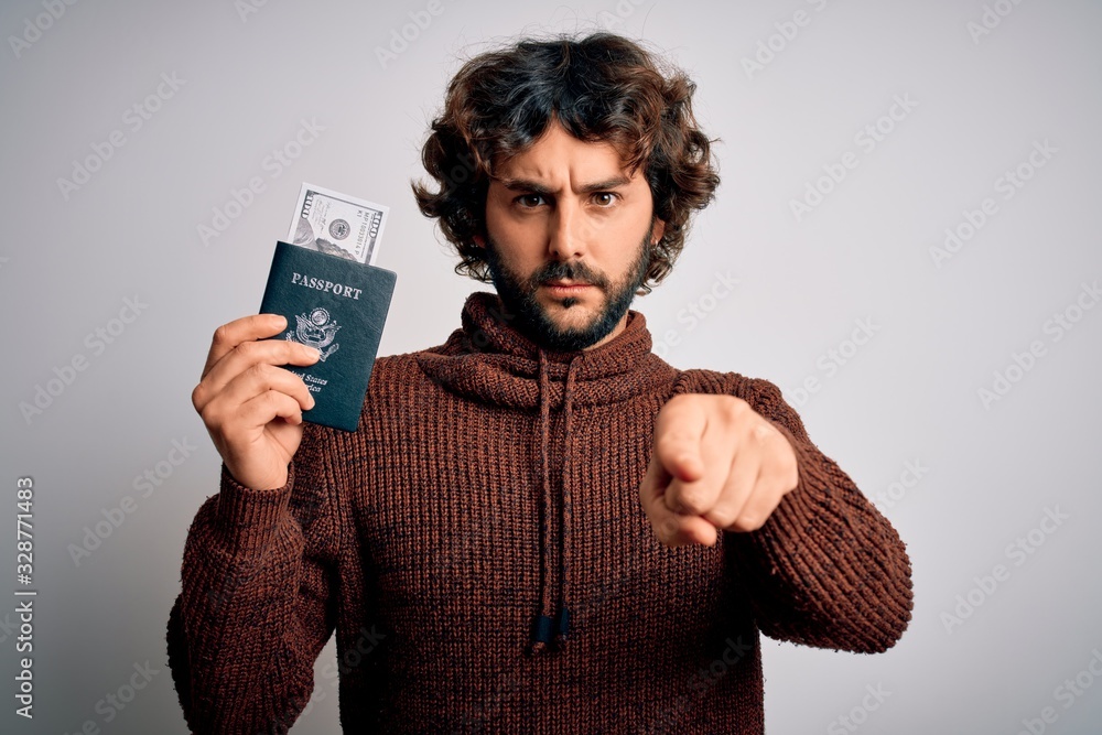 Handsome tourist man with beard holding passport with dollars banknotes as money travel pointing with finger to the camera and to you, hand sign, positive and confident gesture from the front Handsome tourist man with beard holding passport with dollars banknotes as money travel pointing with finger to the camera and to you, hand sign, positive and confident gesture from the front