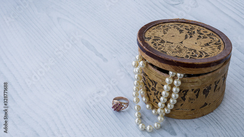 Old wooden jewerly box with pearl necklace. Golden ring with purple natural stones close to fashion brown trunk for bijoutery. Isolated on the white wooden background. photo