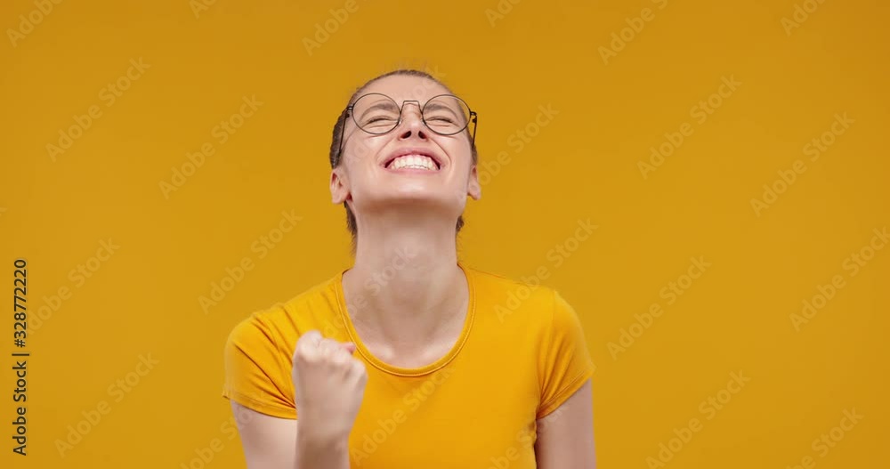 Young pretty fan girl shouting while her team wins, raised fist in victory gesture, isolated on studio yellow background Young pretty fan girl shouting while her team wins, raised fist in victory gesture, isolated on studio yellow background