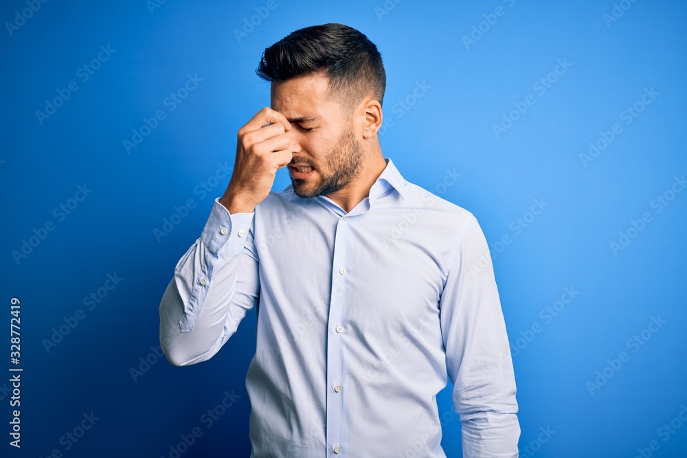 Young handsome man wearing elegant shirt standing over isolated blue background tired rubbing nose and eyes feeling fatigue and headache. Stress and frustration concept. Young handsome man wearing elegant shirt standing over isolated blue background tired rubbing nose and eyes feeling fatigue and headache. Stress and frustration concept.