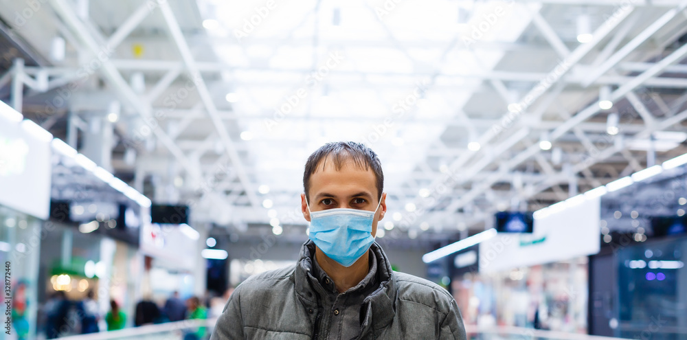 A young man in a medical mask in a shopping center. The masked man protects himself from the epidemic of the Chinese virus 