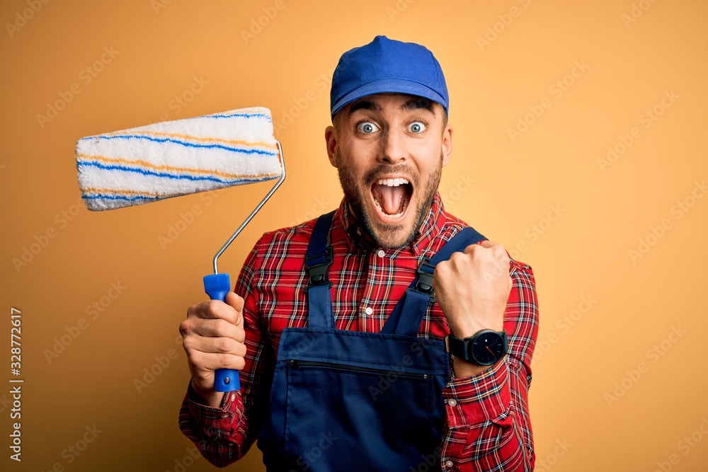 Young handsome painter man painting wall using roller over isolated yellow  background screaming proud and celebrating victory and success very  excited, cheering emotion Stock Photo | Adobe Stock