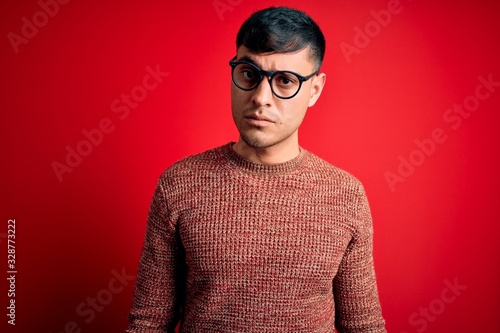 Young handsome hispanic man wearing nerd glasses over red background skeptic and nervous, frowning upset because of problem. Negative person.