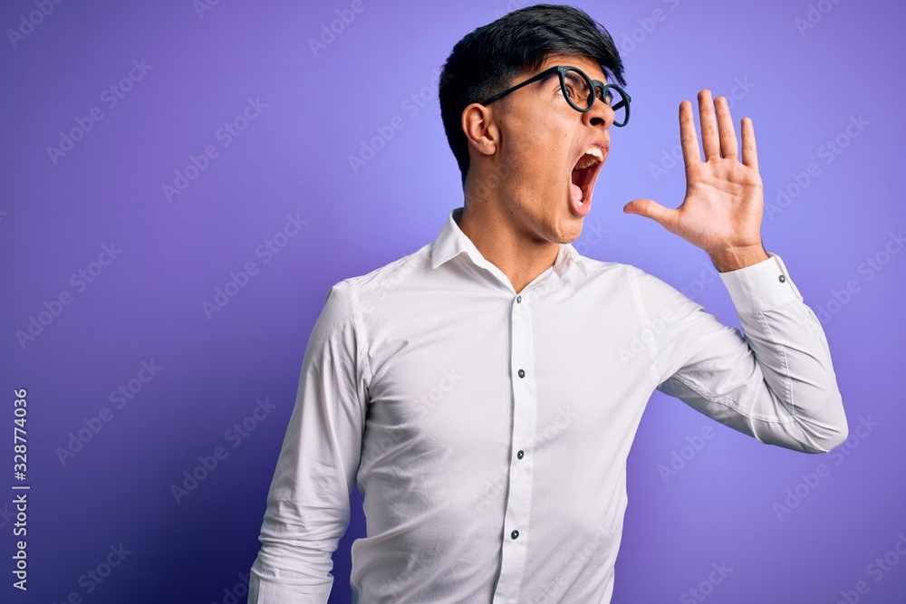Young handsome business man wearing shirt and glasses over isolated purple background shouting and screaming loud to side with hand on mouth. Communication concept. Young handsome business man wearing shirt and glasses over isolated purple background shouting and screaming loud to side with hand on mouth. Communication concept.