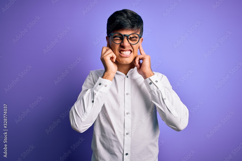 Young handsome business man wearing shirt and glasses over isolated purple background covering ears with fingers with annoyed expression for the noise of loud music. Deaf concept. Young handsome business man wearing shirt and glasses over isolated purple background covering ears with fingers with annoyed expression for the noise of loud music. Deaf concept.