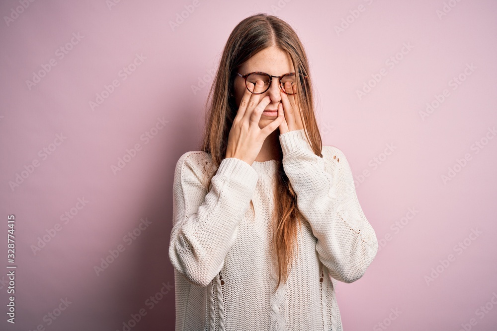 Young beautiful redhead woman wearing casual sweater and glasses over pink background rubbing eyes for fatigue and headache, sleepy and tired expression. Vision problem Young beautiful redhead woman wearing casual sweater and glasses over pink background rubbing eyes for fatigue and headache, sleepy and tired expression. Vision problem