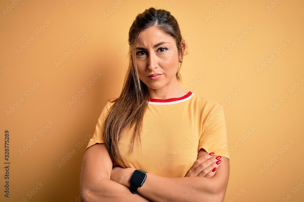 Obraz premium Young beautiful athletic woman wearing casual t-shirt and ponytail over yellow background skeptic and nervous, disapproving expression on face with crossed arms. Negative person.