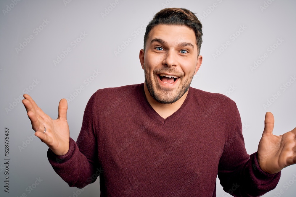Young man with blue eyes wearing casual sweater standing over isolated background celebrating crazy and amazed for success with arms raised and open eyes screaming excited. Winner concept Young man with blue eyes wearing casual sweater standing over isolated background celebrating crazy and amazed for success with arms raised and open eyes screaming excited. Winner concept
