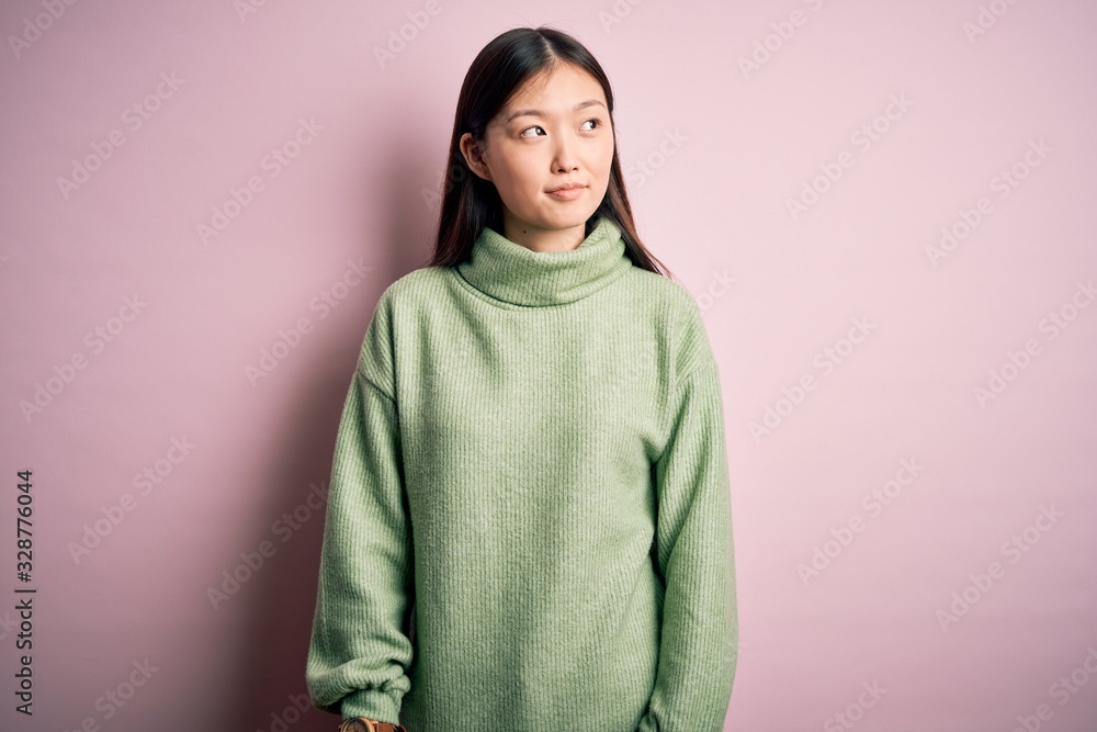 Fototapeta premium Young beautiful asian woman wearing green winter sweater over pink solated background smiling looking to the side and staring away thinking.