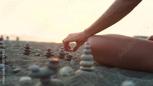 Woman practicing yoga on the beach. Balance ang relax. Tanned slim girl collects stones. Relaxation and yoga exercises on the beach.