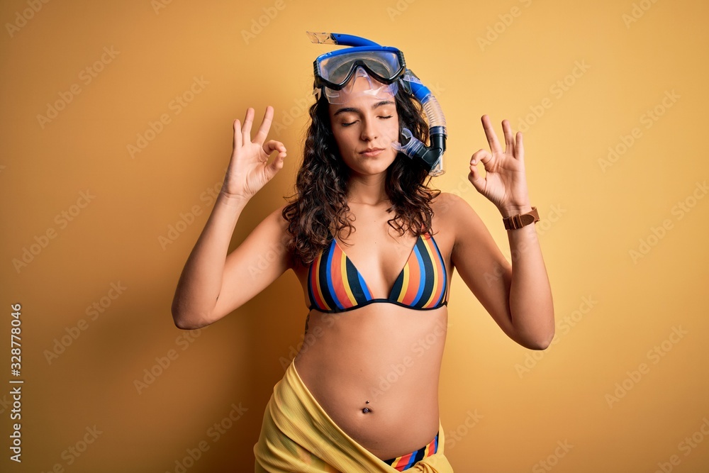 Young beautiful woman with curly hair on vacation wearing bikini and diving googles relax and smiling with eyes closed doing meditation gesture with fingers. Yoga concept. Young beautiful woman with curly hair on vacation wearing bikini and diving googles relax and smiling with eyes closed doing meditation gesture with fingers. Yoga concept.