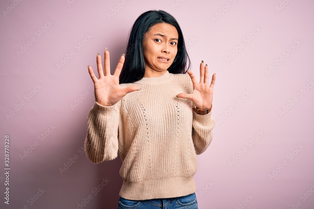 Young beautiful chinese woman wearing casual sweater over isolated pink background afraid and terrified with fear expression stop gesture with hands, shouting in shock. Panic concept. Young beautiful chinese woman wearing casual sweater over isolated pink background afraid and terrified with fear expression stop gesture with hands, shouting in shock. Panic concept.