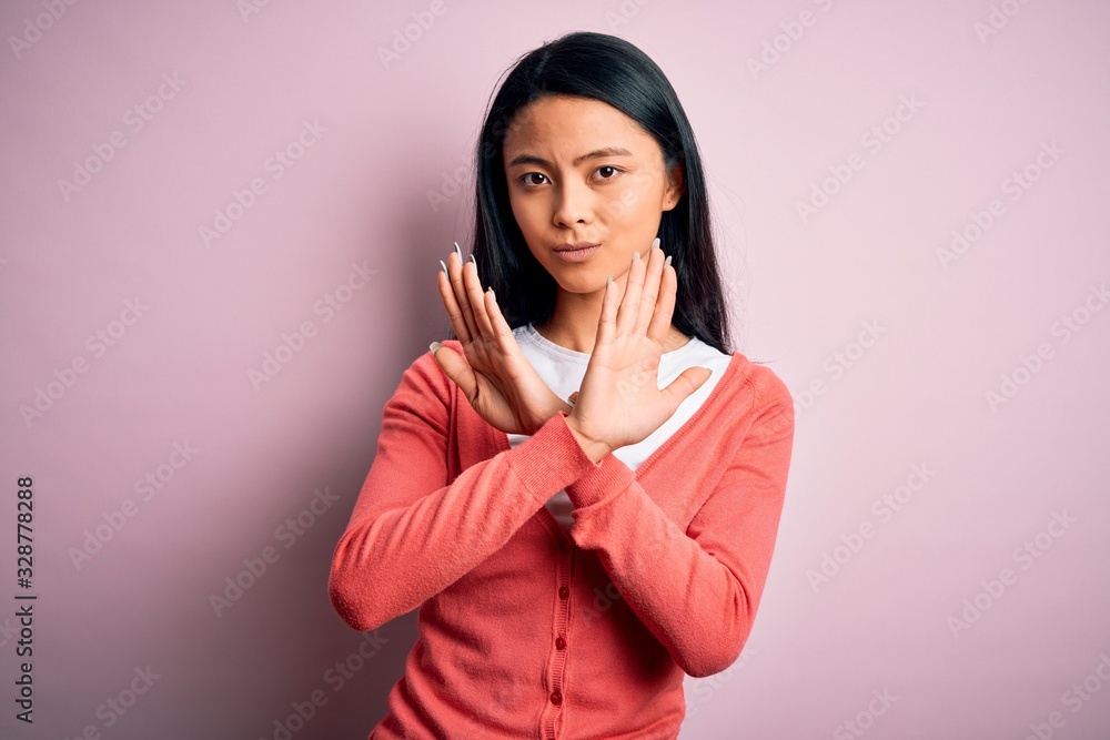 Young beautiful chinese woman wearing casual sweater over isolated pink background Rejection expression crossing arms doing negative sign, angry face Young beautiful chinese woman wearing casual sweater over isolated pink background Rejection expression crossing arms doing negative sign, angry face