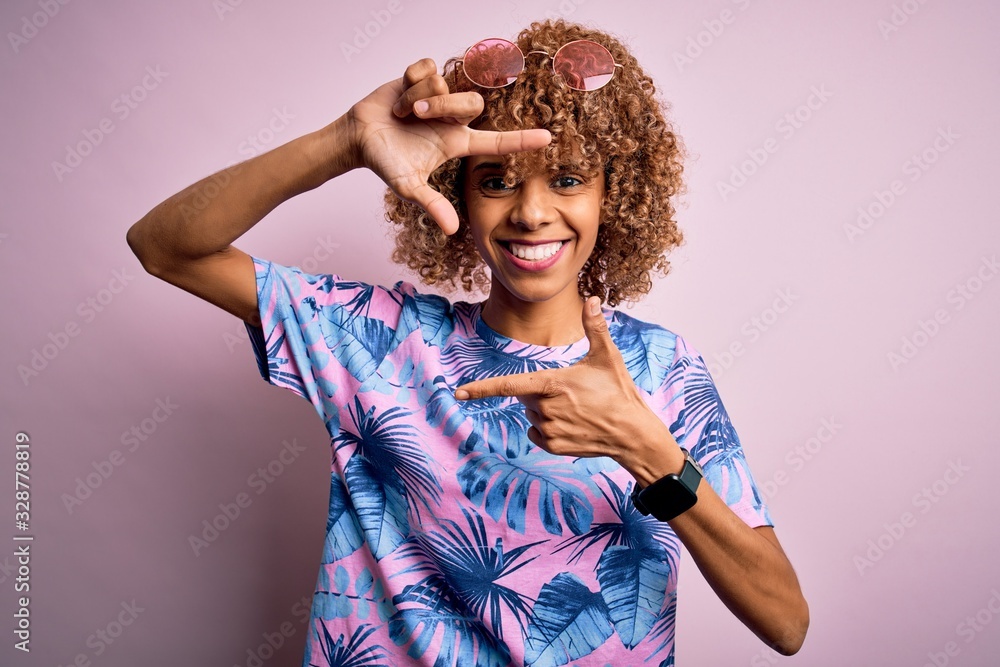 Young african american woman on vacation wearing summer t-shirt over pink background smiling making frame with hands and fingers with happy face. Creativity and photography concept. Young african american woman on vacation wearing summer t-shirt over pink background smiling making frame with hands and fingers with happy face. Creativity and photography concept.