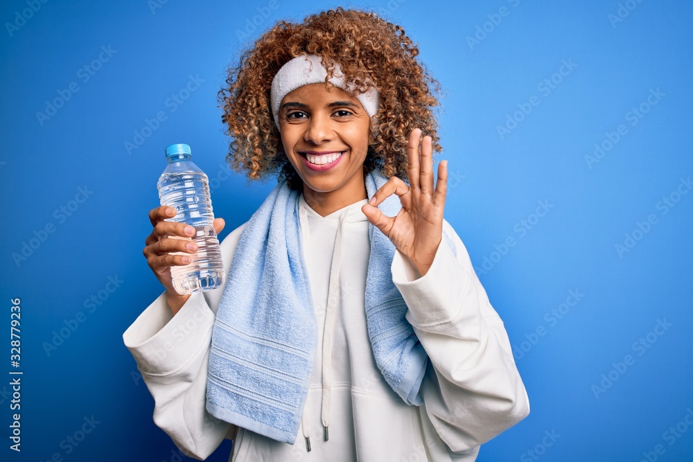 Young african american sportswoman doing sport wearing towel drinking botte of water doing ok sign with fingers, excellent symbol Young african american sportswoman doing sport wearing towel drinking botte of water doing ok sign with fingers, excellent symbol