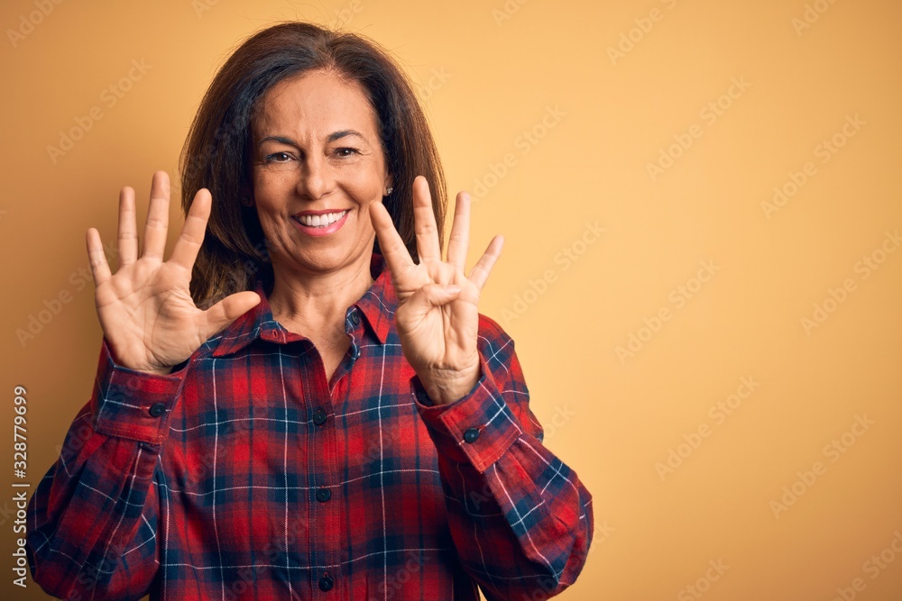 Middle age beautiful woman wearing casual shirt standing over isolated yellow background showing and pointing up with fingers number nine while smiling confident and happy. Middle age beautiful woman wearing casual shirt standing over isolated yellow background showing and pointing up with fingers number nine while smiling confident and happy.
